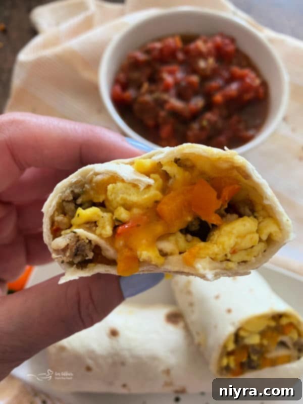 A breakfast burrito cut in half, showing the rich filling of sausage, egg, cheese, and vegetables.