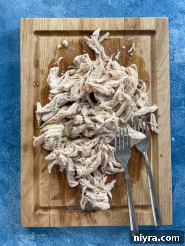 Shredded chicken with fork on wooden cutting board