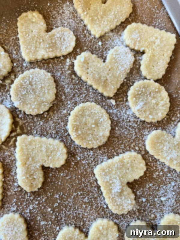 Sprinkling cinnamon sugar over pie crust cookies on a baking sheet before baking.