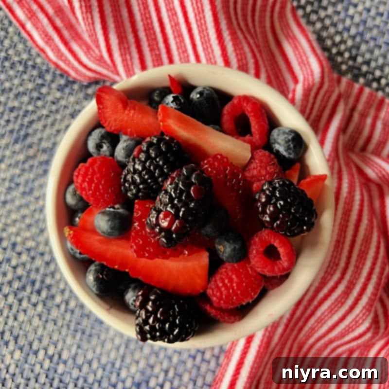 Assortment of fresh berries (blueberries, blackberries, strawberries, raspberries) in a white bowl.