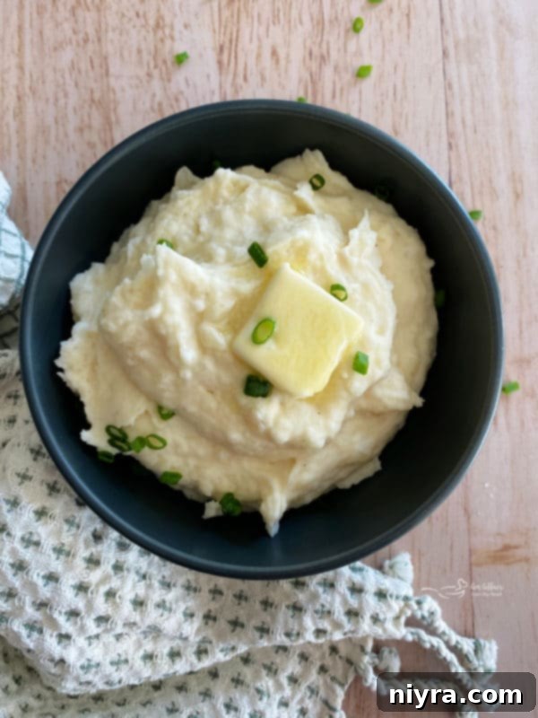Top view of mashed potatoes in black bowl with chives and butter, showcasing creamy texture.