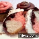 Triple Treat Neapolitan Cupcakes 2 Neapolitan Cupcakes and one cut in half on a white surface