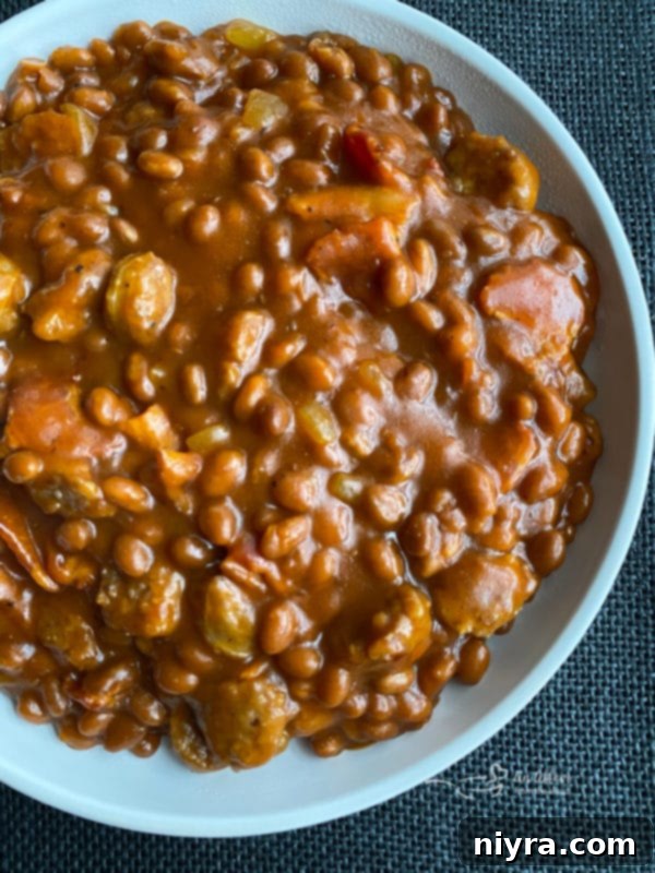 Hearty Meat Lovers Baked Beans with bacon and bratwurst in a rustic bowl, garnished with fresh herbs