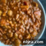 Meat Lovers Baked Beans in a white bowl with a serving spoon