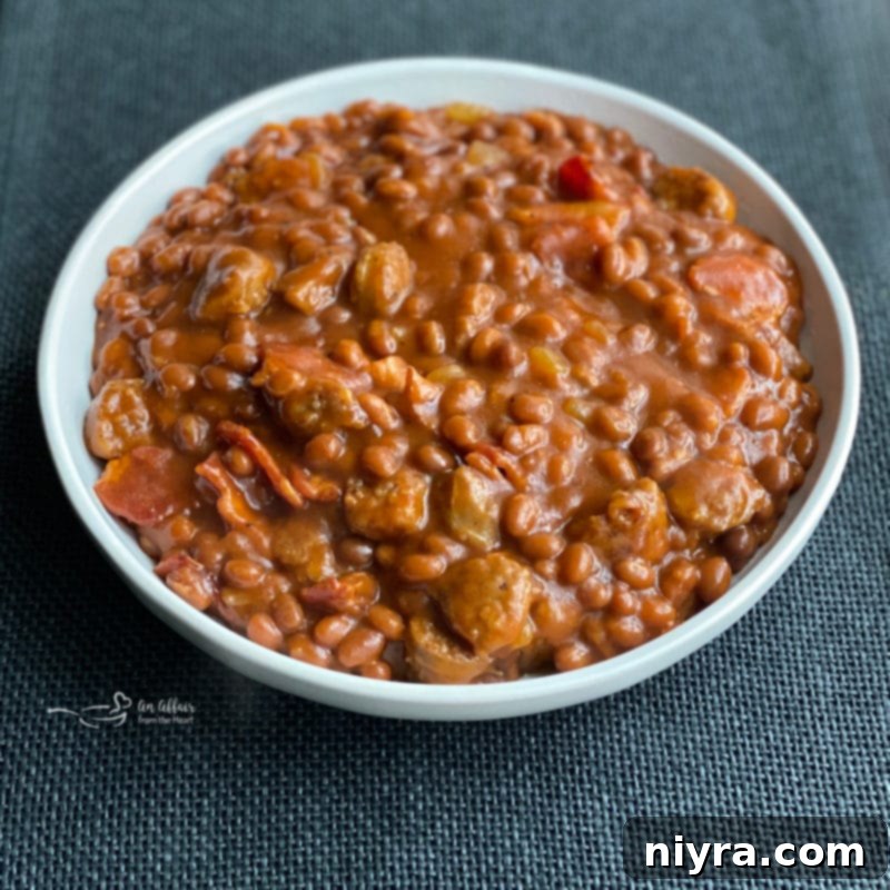 A generous serving of Meat Lovers Baked Beans with visible pieces of bratwurst and bacon in a rustic bowl