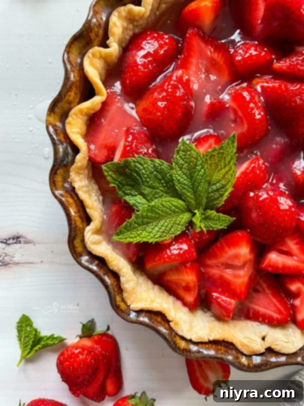 Top view of a freshly baked strawberry pie, garnished with a sprig of mint, highlighting its vibrant color and inviting texture.