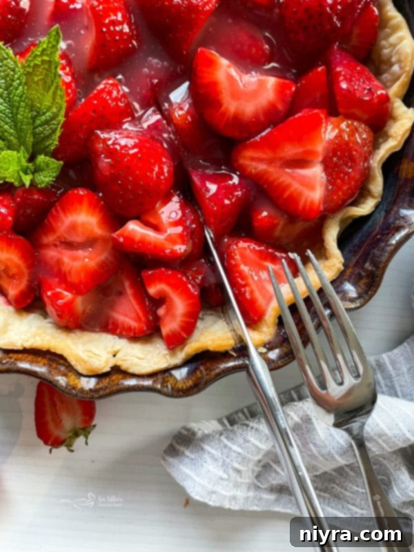 Top view of a whole fresh strawberry pie, with a serving knife and fork placed nearby, highlighting its beautiful presentation and readiness for enjoyment.