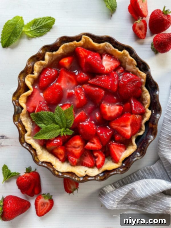 A close-up top view of a freshly baked strawberry pie, adorned with delicate mint sprigs, showcasing its vibrant red filling and golden crust.