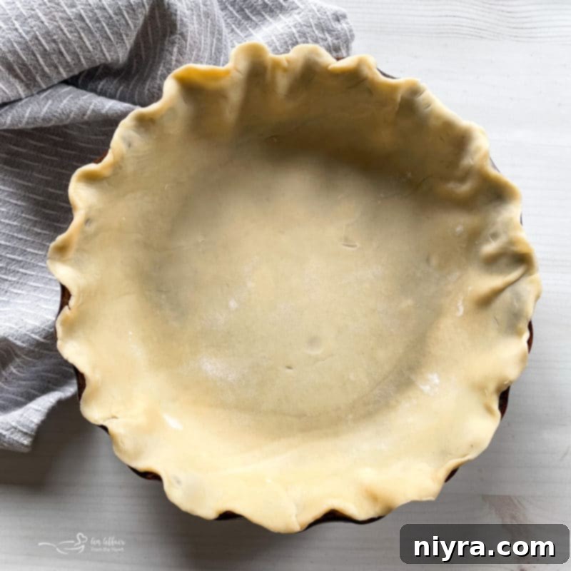 Hands gently working pie dough into a firm ball on a lightly floured surface, indicating the next step in making a homemade pie crust.