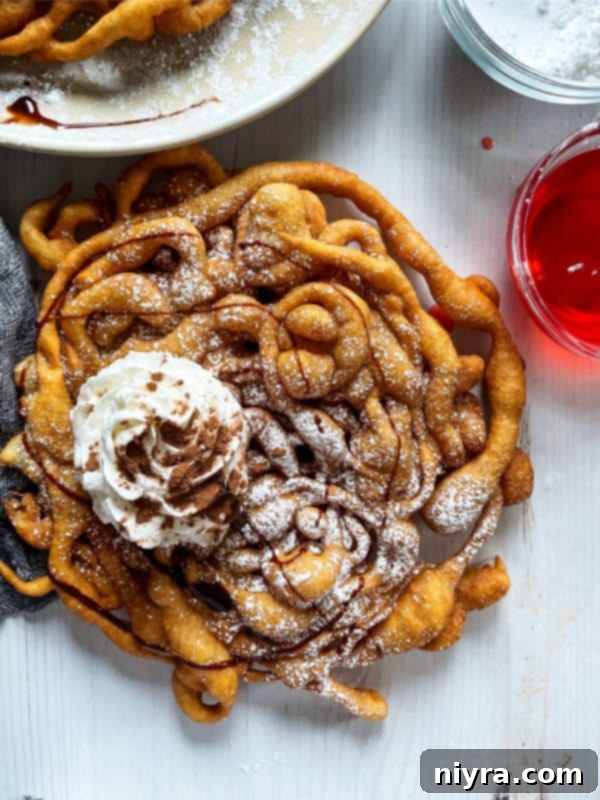 Top view of a homemade funnel cake topped with whipped cream and chocolate drizzle on a white surface, ready to be enjoyed.