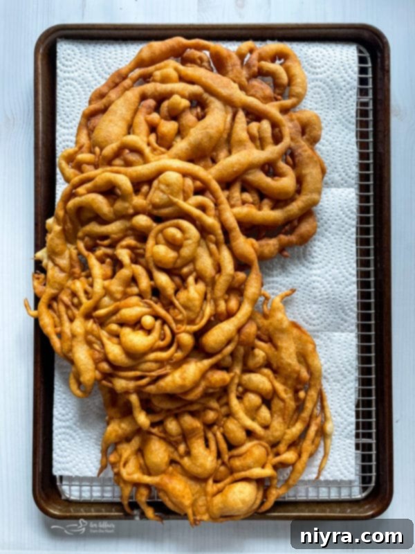Several freshly fried golden-brown funnel cakes resting on a paper towel-lined baking sheet, draining excess oil.