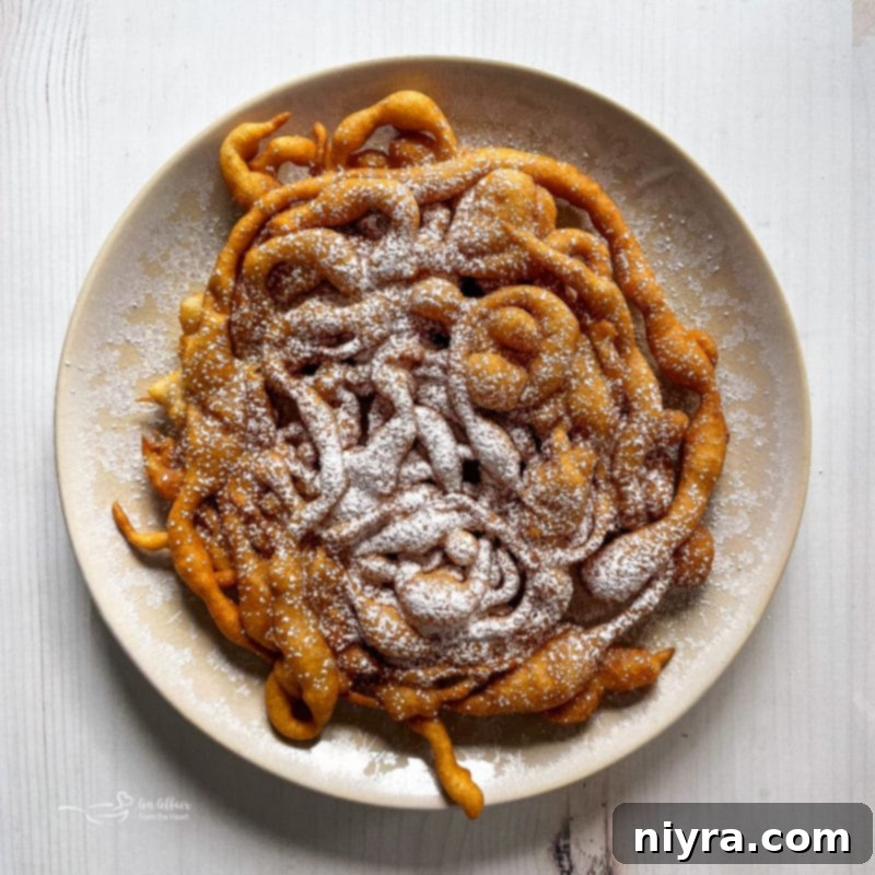 A stack of warm, golden-brown funnel cakes generously sprinkled with powdered sugar on a white plate, ready to be enjoyed.
