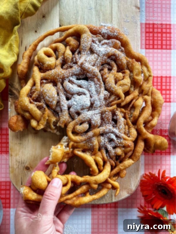 A hand gently pulling apart a piece of freshly fried homemade funnel cake, highlighting its crispy texture.