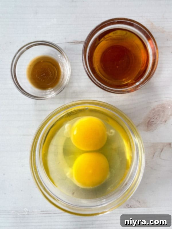 Close-up of wet ingredients for funnel cake: eggs, vanilla extract, and maple syrup, perfectly measured in small bowls.