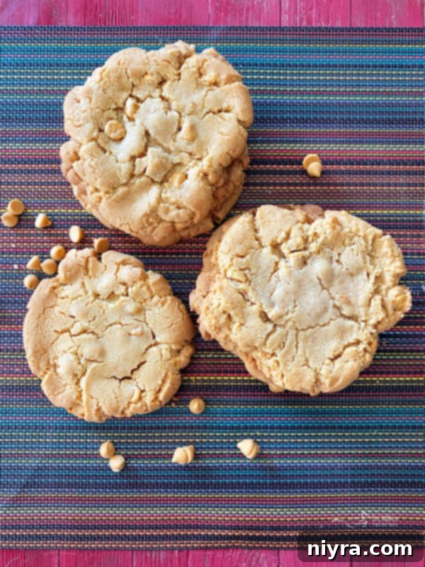 Mega Butterscotch Cookies 2 Three golden-brown giant butterscotch cookies stacked on a rustic wooden surface, showcasing their size and inviting texture.