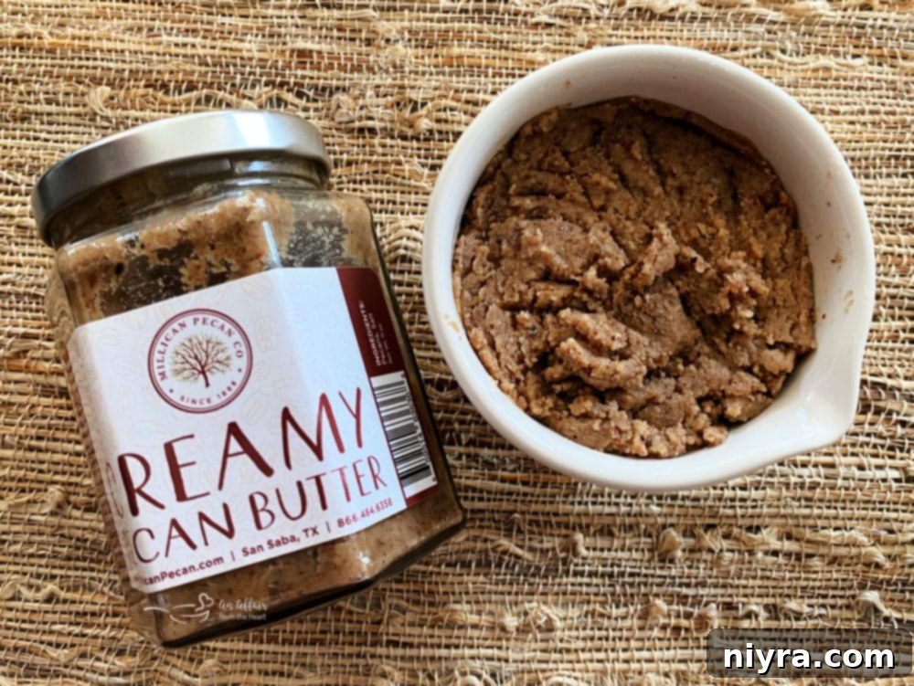 A rustic jar of creamy pecan butter sits alongside a small bowl of whole pecans, hinting at the key ingredient used in the cookies.