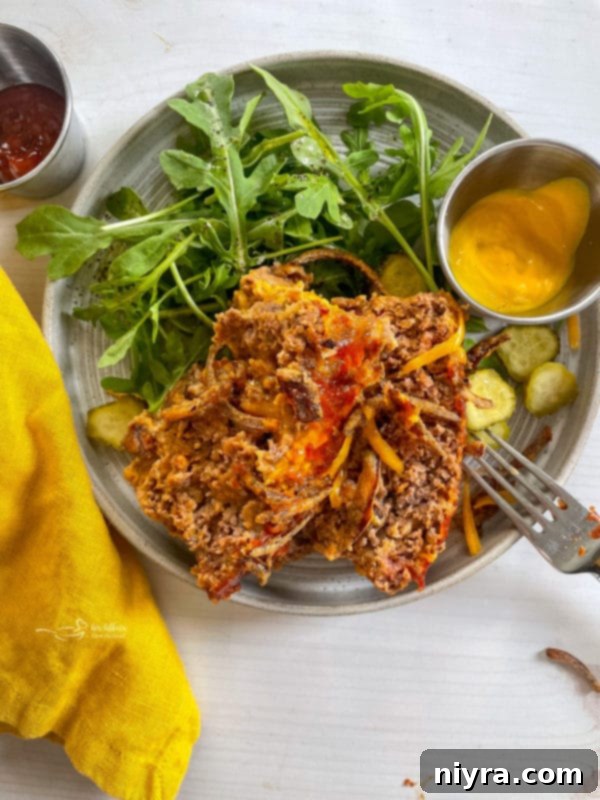 A slice of Bacon Cheeseburger Meatloaf on a plate with a fresh green salad and a dollop of mustard, ready to be enjoyed.