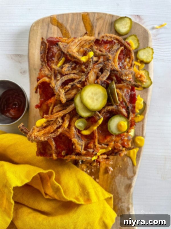 A serving of Bacon Cheeseburger Meatloaf garnished with crispy fried onions and fresh dill pickles, highlighting its burger-inspired toppings.