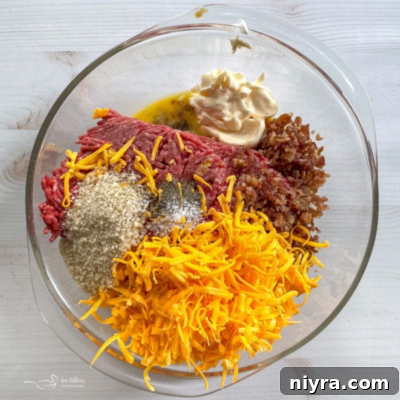 A large mixing bowl filled with the raw ingredients for meatloaf, including ground beef, grated cheese, crumbled bacon, breadcrumbs, eggs, mayonnaise, mustard, salt, and pepper, ready for mixing.