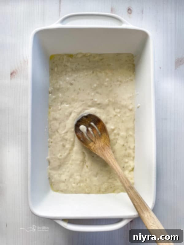 Cheesy Potatoes Au Gratin spreading sauce in bottom layer of baking dish with spoon