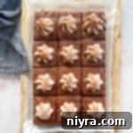 Mexican chocolate frosted brownies sliced and topped with cinnamon whipped cream, on a wood board.