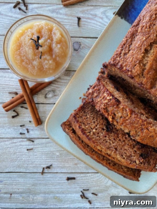 A single loaf of moist applesauce bread with chocolate chips, served on a plate next to a bowl of applesauce and cinnamon sticks, highlighting its rich, golden-brown crust.