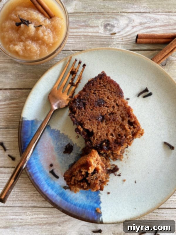 A single slice of moist applesauce bread with chocolate chips, presented on a white plate with a fork, ready to be savored.