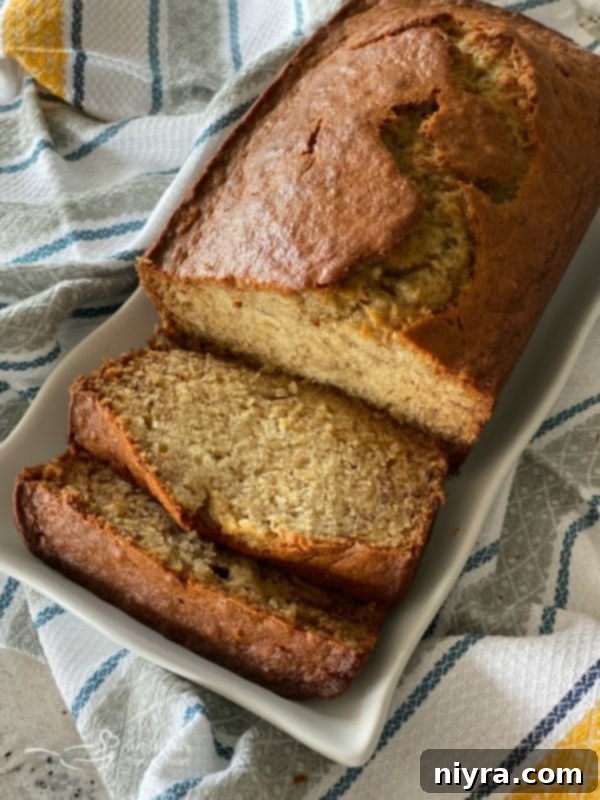Overhead shot of a beautifully baked loaf of 'The BEST Banana Bread' on a white platter, tempting with its golden crust and moist interior.