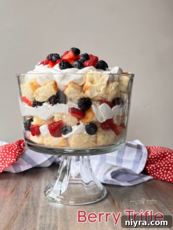 A stunning Triple Berry Trifle in a clear glass pedestal bowl, beautifully garnished