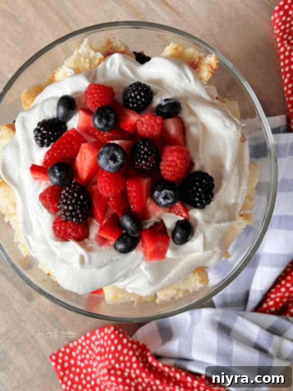 Decorating the top of a Berry Trifle with remaining cake cubes, whipped cream, and fresh berries