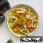 Close up of Homemade Chicken Noodle Soup and a spoon in a white bowl.
