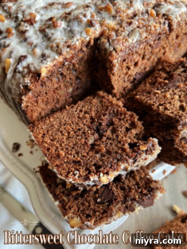 A whole Bittersweet Chocolate Coffee Cake on a white marble surface, dusted with powdered sugar and drizzled with icing.