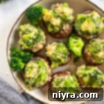 A close-up of a plate of broccoli stuffed mushrooms, showcasing the cheesy filling and golden-brown caps.
