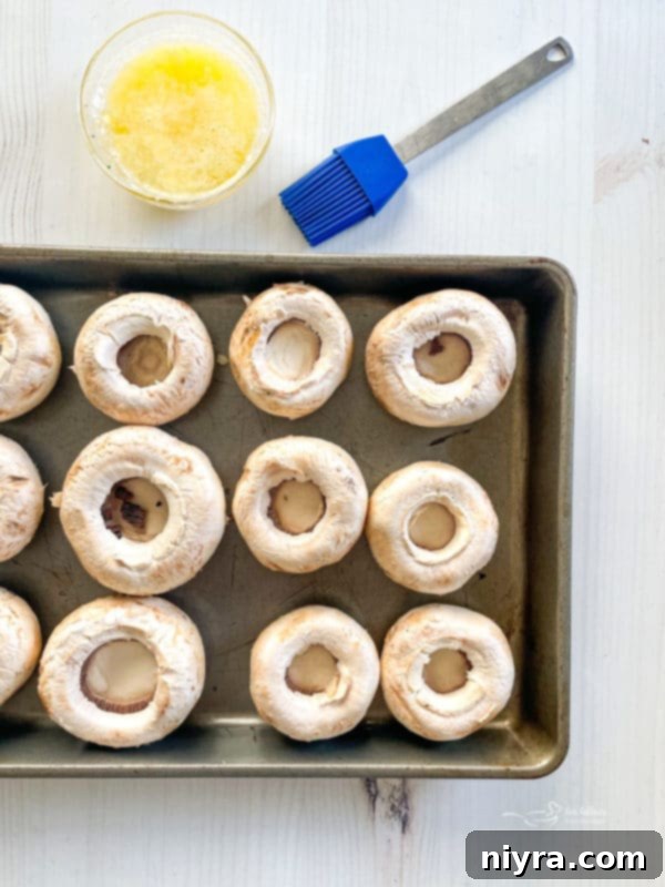 Empty mushroom caps brushed with butter on a baking sheet, ready for filling.