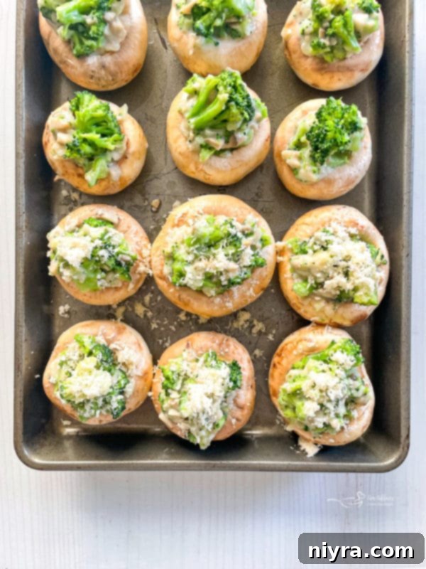 Mushroom caps on a baking tray, stuffed with the broccoli and cheese mixture.