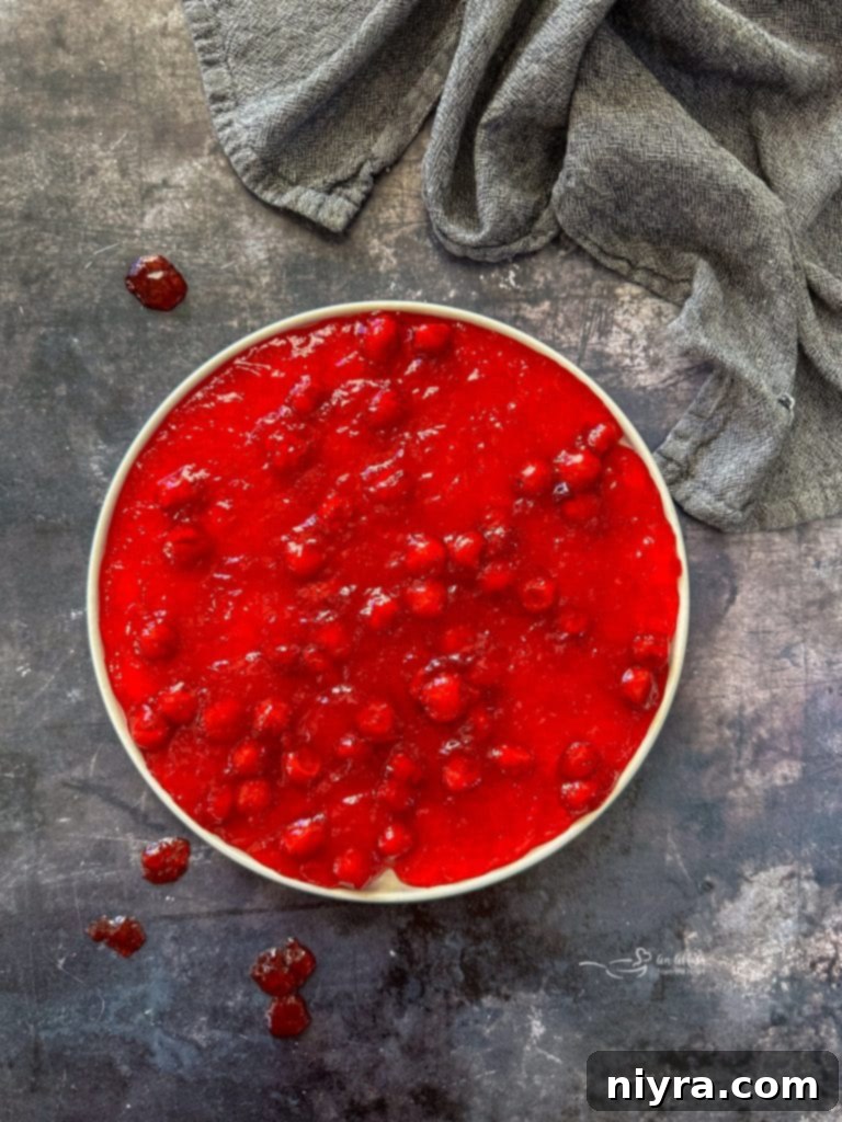 A festive red Cherry Pie Jell-O Salad in a clear glass bowl, garnished with a few fresh cherries.