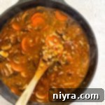 Stirring the Vegetable Beef Barley Soup with Mushrooms in the pot.