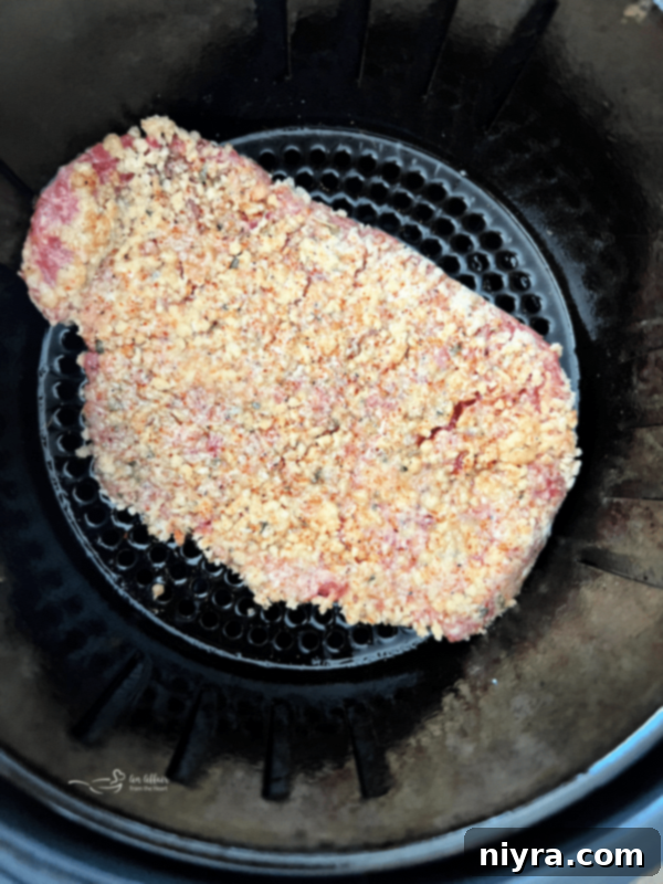 Air fryer basket being sprayed with non-stick cooking spray before placing steaks inside.