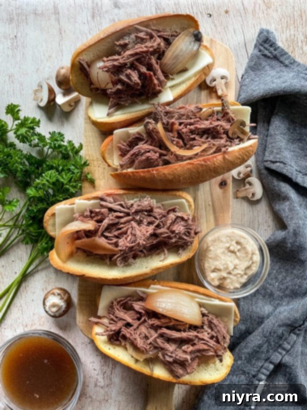 Top view of French Onion French Dip sandwiches arranged neatly on a wooden cutting board, garnished with fresh herbs and a small bowl of au jus for dipping.