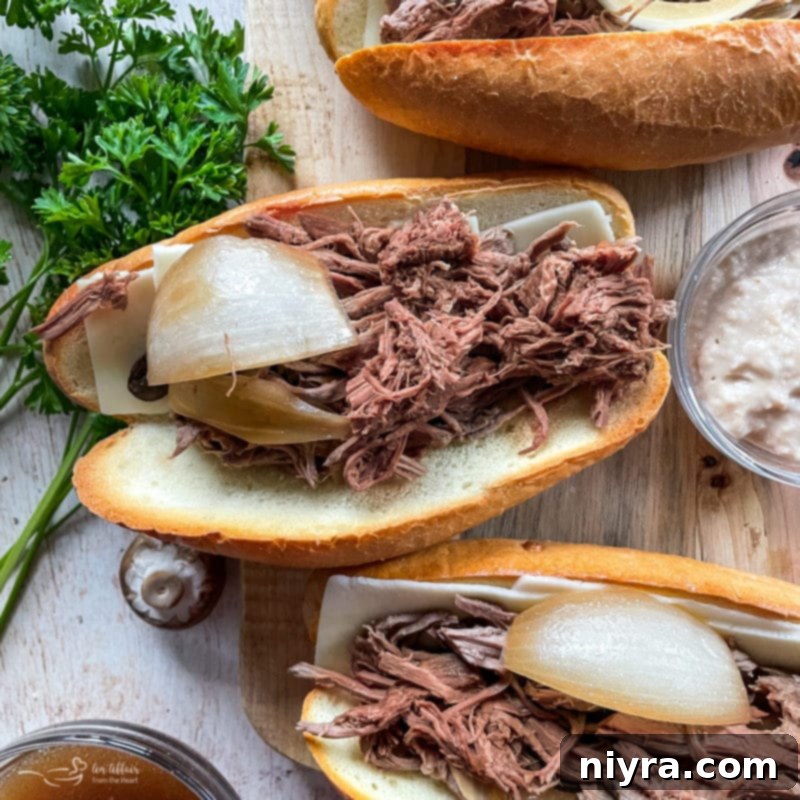 A freshly assembled French Dip sandwich with tender shredded beef and melted cheese, resting on a toasted hoagie roll, ready to be served with au jus.