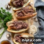 Top view of four French Dip sandwiches on a wooden cutting board, ready to be served with au jus.