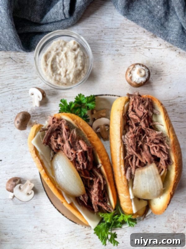 Two perfectly assembled French Onion French Dip sandwiches, showcasing the tender beef and melted cheese, ready for dipping into the rich au jus.