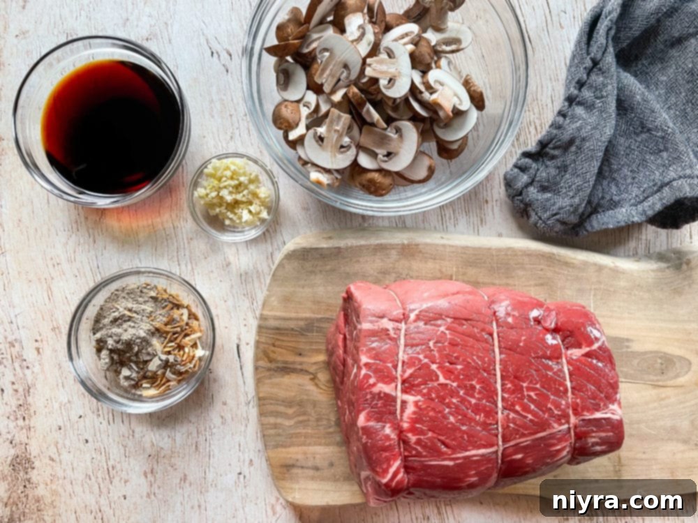 A selection of French Dip sandwich ingredients laid out: raw beef chuck roast, fresh mushrooms, a bottle of soy sauce, garlic cloves, and a seasoning packet.