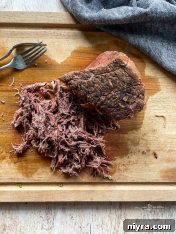 Shredded tender beef chuck roast on a wooden cutting board, pulled apart after slow cooking.