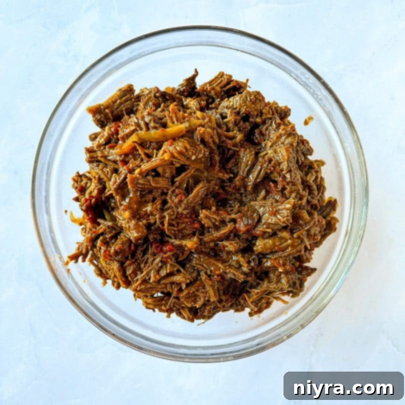 A close-up of a steaming Crock Pot filled with slow-cooked shredded beef, ready to be prepared for burritos.