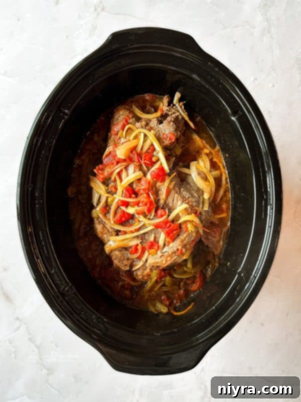 Close-up of perfectly shredded beef in a slow cooker, swimming in a rich, flavorful sauce, ready to be served in burritos.