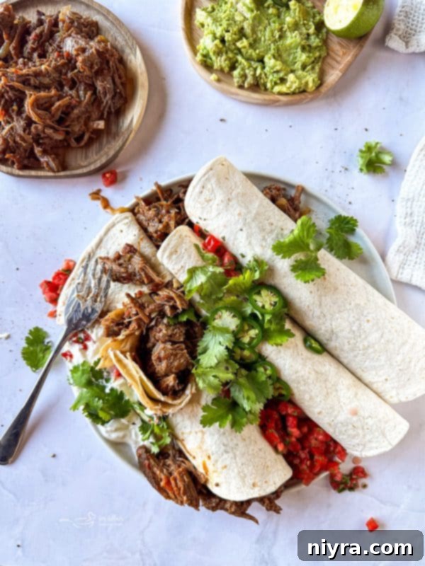 A spread of delicious Crock Pot Shredded Beef Burritos, some unwrapped to show the juicy filling, alongside fresh cilantro and lime wedges.