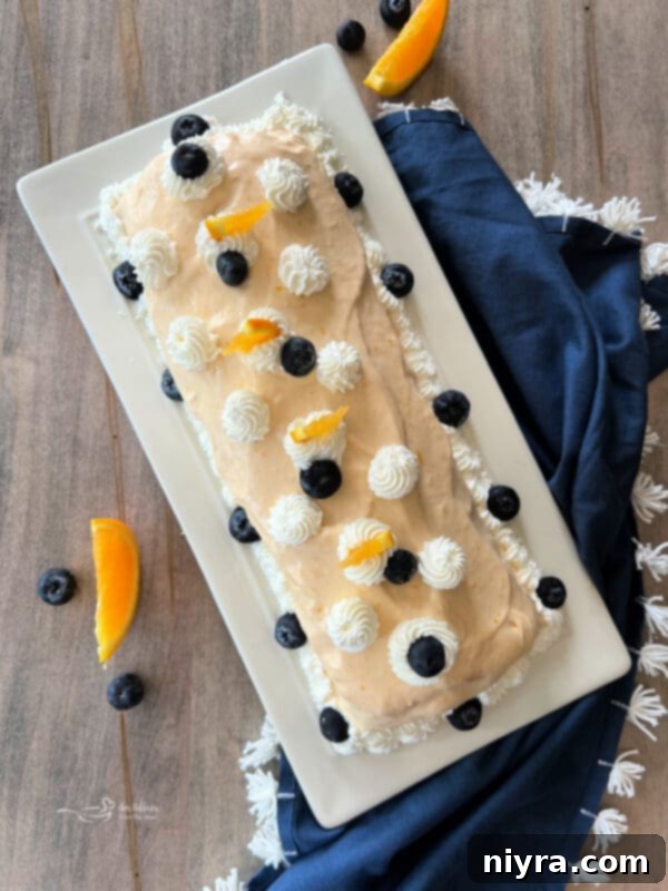 Finished Blueberry Orange Angel Food Cake Roll beautifully frosted with orange cream cheese and garnished with fresh fruit