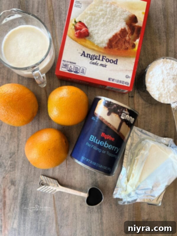 A selection of fresh ingredients including oranges, blueberries, cream cheese, and a box of angel food cake mix, laid out for baking
