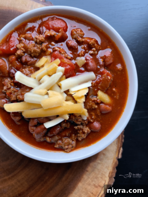 A bowl of Three Bean Chili, garnished with shredded cheese and a dollop of sour cream, served with a side of cornbread.